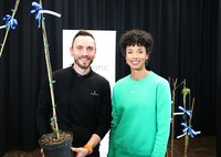 Daniel Lüttger hält einen Apfelbaum in der Hand, daneben steht Olympiasiegerin Malaika Mihambo