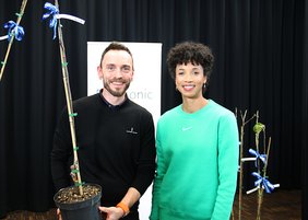 Daniel Lüttger hält einen Apfelbaum in der Hand, daneben steht Olympiasiegerin Malaika Mihambo
