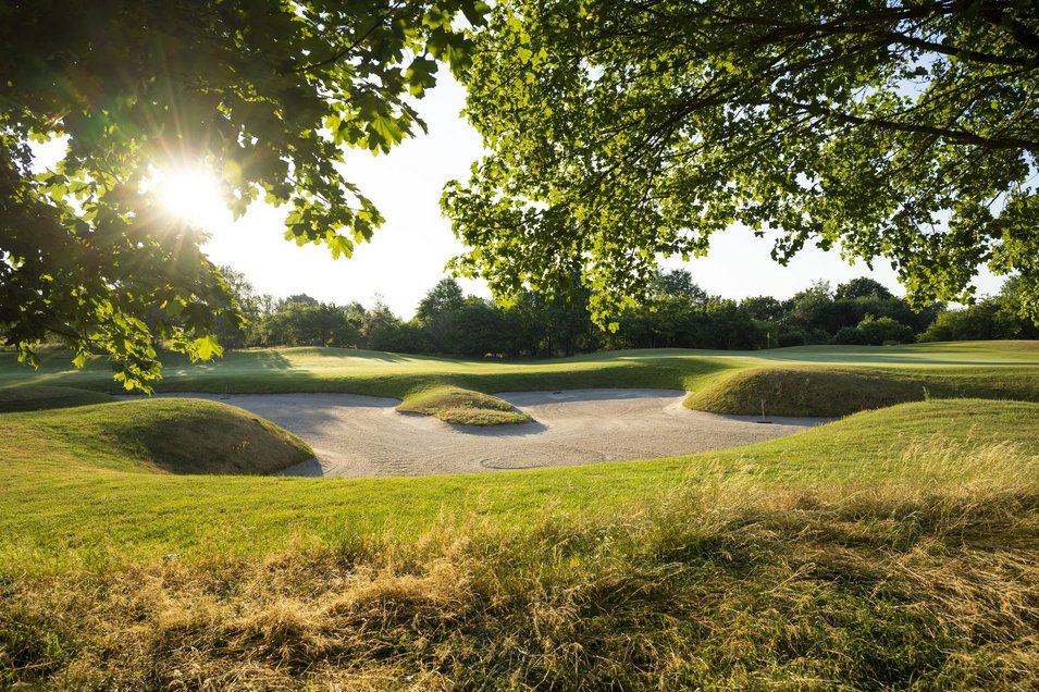 Golfbunker bei Sonnenschein mit grüner Wiese im Vordergrund