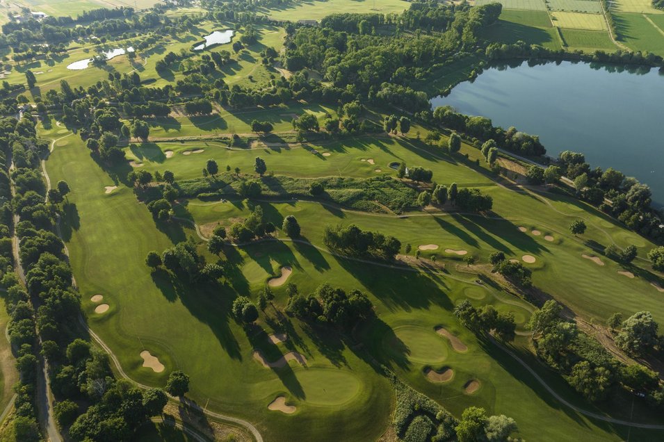 Luftaufnahme von Golfplatz mit verschiedenen Spielbahnen, Bäumen und Baggersee auf rechter Seite
