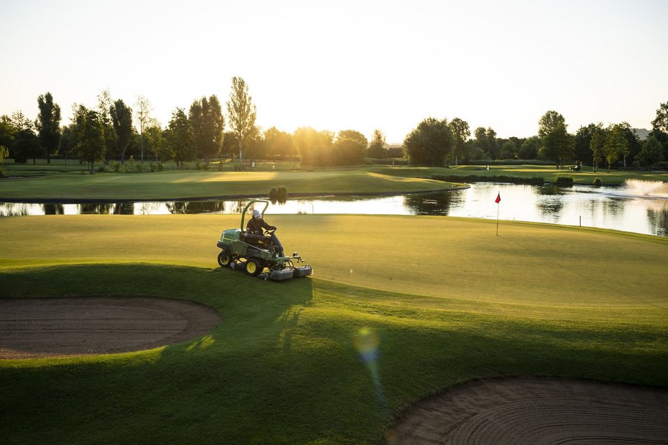 Rasenmäher mit untergehender Sonne und Teich im Hintergrund