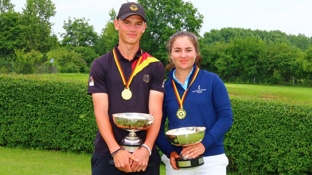 Tjelle Rieger im schwarzen Poloshirt steht neben Sofia Maier-Borst im blauen Langarmshirt jeweils mit Pokal in der Hand